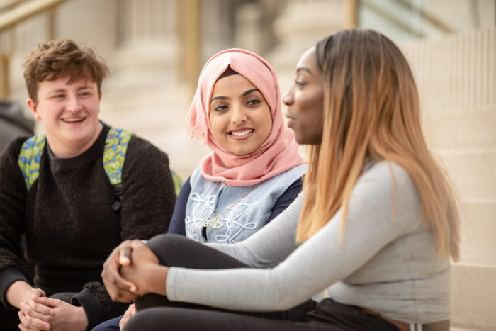 Three students sit and talk on some steps.