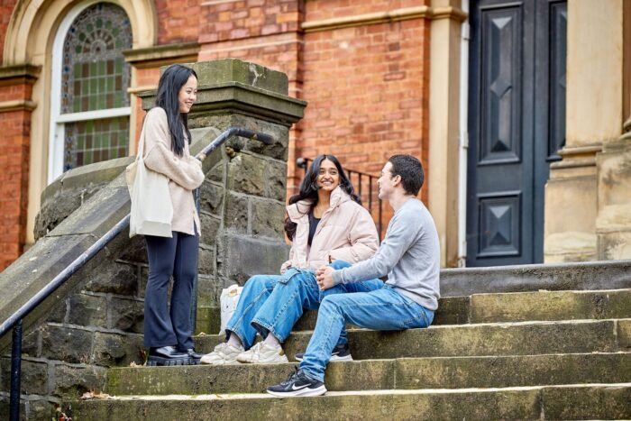 Three people sit on stairs outside of an old building.