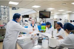 Students sitting around a table in a food science lab with various equipment laid out in front of them.